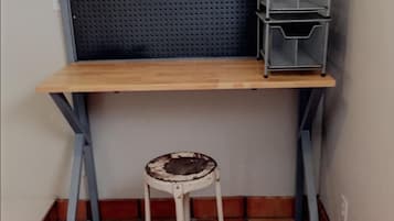 Un espacio de trabajo en esquina con un escritorio de madera, panel posterior de malla metálica y un taburete blanco.