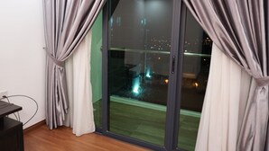 A room with a sliding glass door leading to a balcony, a desk, and a power outlet on the wall. - Luco Apartments Viva City Megamall (Kuching)