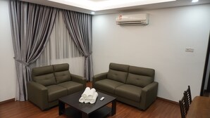 A modern living room with two green sofas, a wooden coffee table with rolled towels, and an air conditioning unit on the wall. - Luco Apartments Viva City Megamall (Kuching)