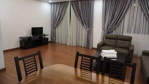 A modern living room with a wooden floor, a dining table with chairs, a sofa, a TV on a stand, and curtains. - Luco Apartments Viva City Megamall (Kuching)