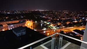 A nighttime cityscape viewed from a high vantage point, featuring a mix of residential and commercial buildings, a prominent curved building, and a well-lit street. - Luco Apartments Viva City Megamall (Kuching)