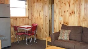 A wooden-paneled room with a dining table and chairs, a sofa, and a refrigerator.