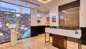 A modern hotel lobby with a digital map display, a reception desk, and a glass partition. - Hub By Premier Inn London - Soho (London)