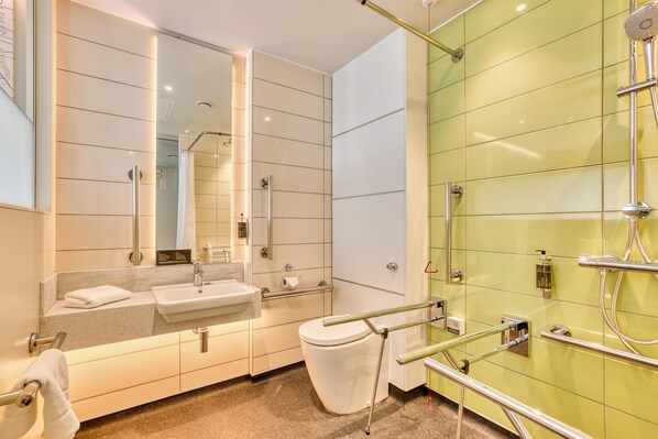 Un baño moderno con lavamanos, inodoro y zona de ducha, que incluye barras de apoyo y un espejo.
