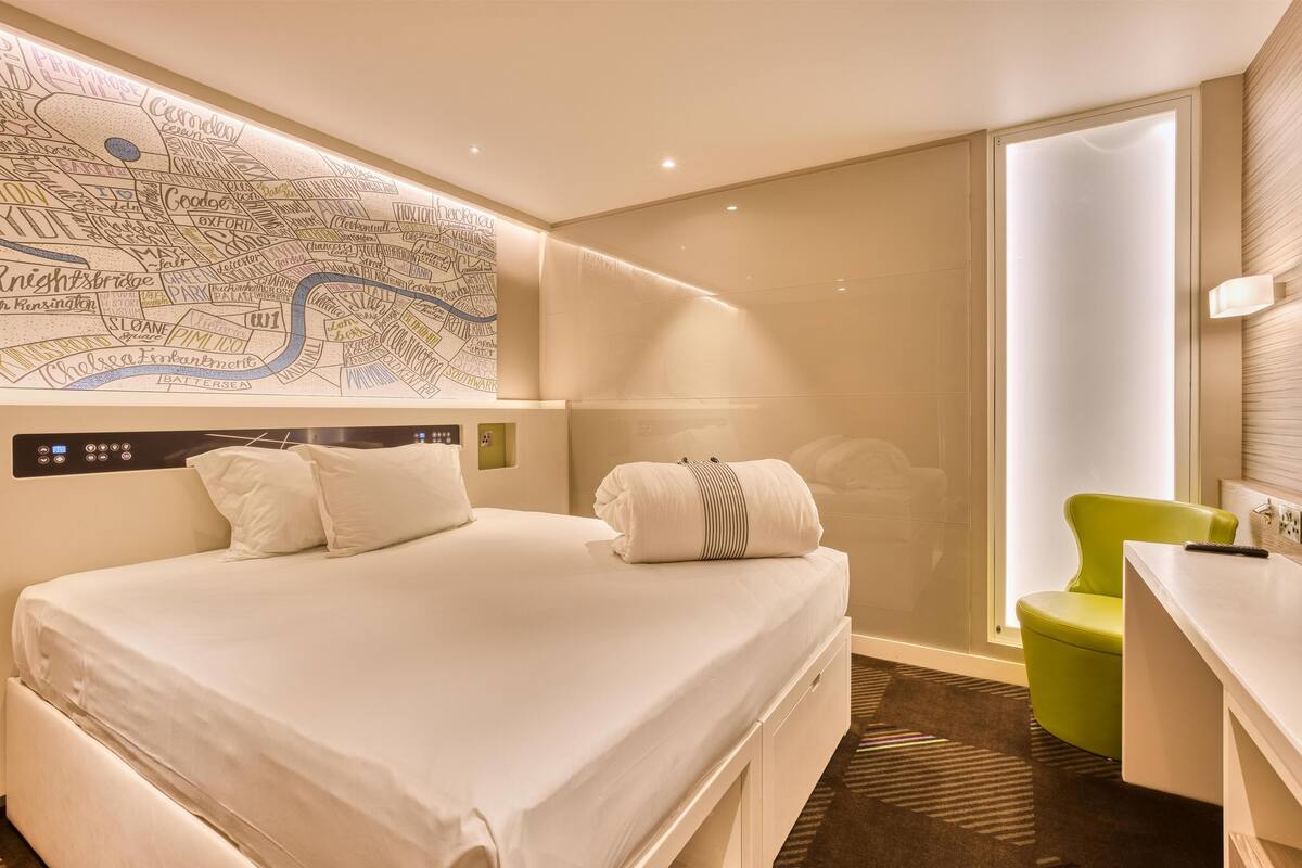 A hotel room with a large bed, a desk, a chair, a map on the wall, and a window.