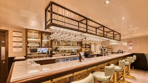 A bar area with a long counter, multiple stools, and a high ceiling with exposed beams. - Hub By Premier Inn London - Soho (London)