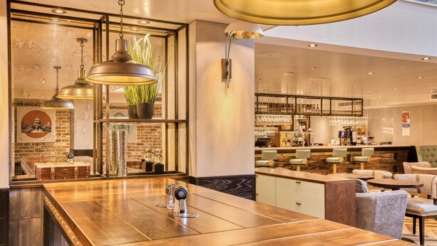 A modern bar area with a wooden bar counter, seating, and a visible wine rack. - Hub By Premier Inn London - Soho (London)