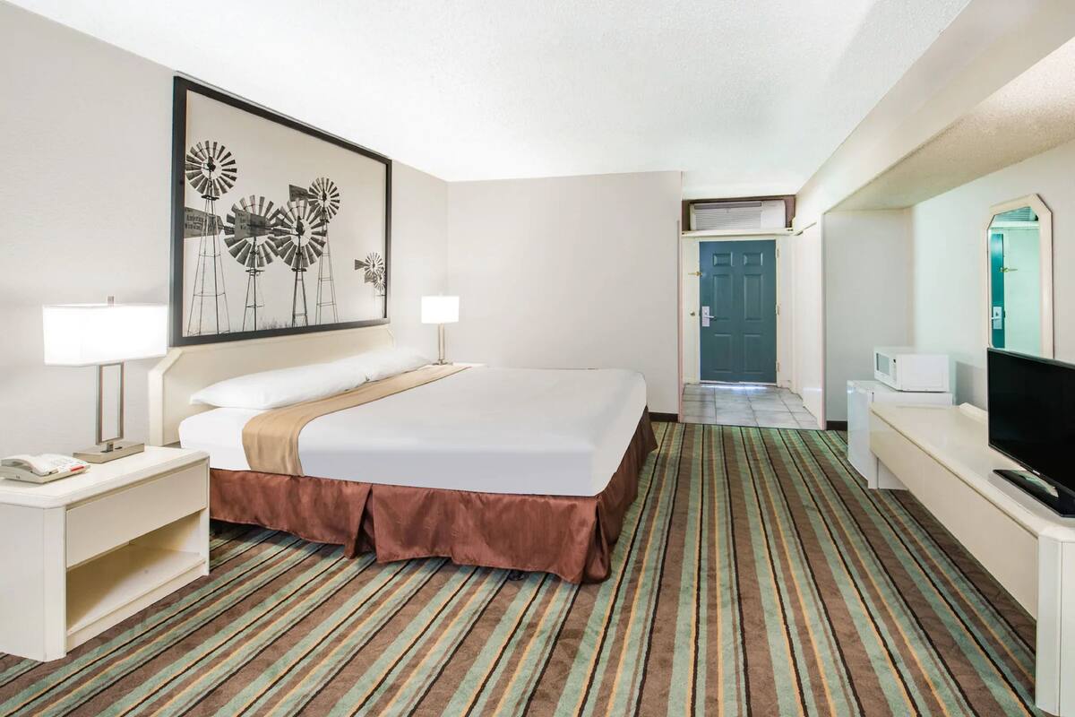 Una habitación de hotel con una cama grande, televisor, escritorio con lámpara y un cuadro enmarcado en la pared.