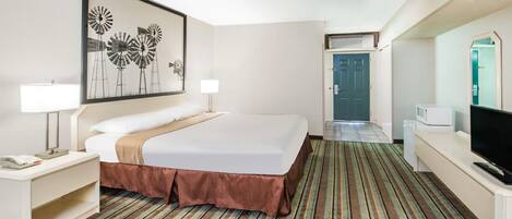 Una habitación de hotel con una cama grande, televisor, escritorio con lámpara y un cuadro enmarcado en la pared.
