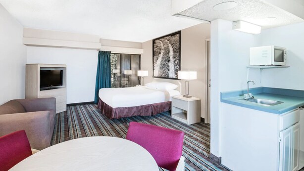 Une chambre d’hôtel comprenant un lit, une télévision, un bureau avec un ordinateur, une petite kitchenette et un coin repas avec une table et des chaises.