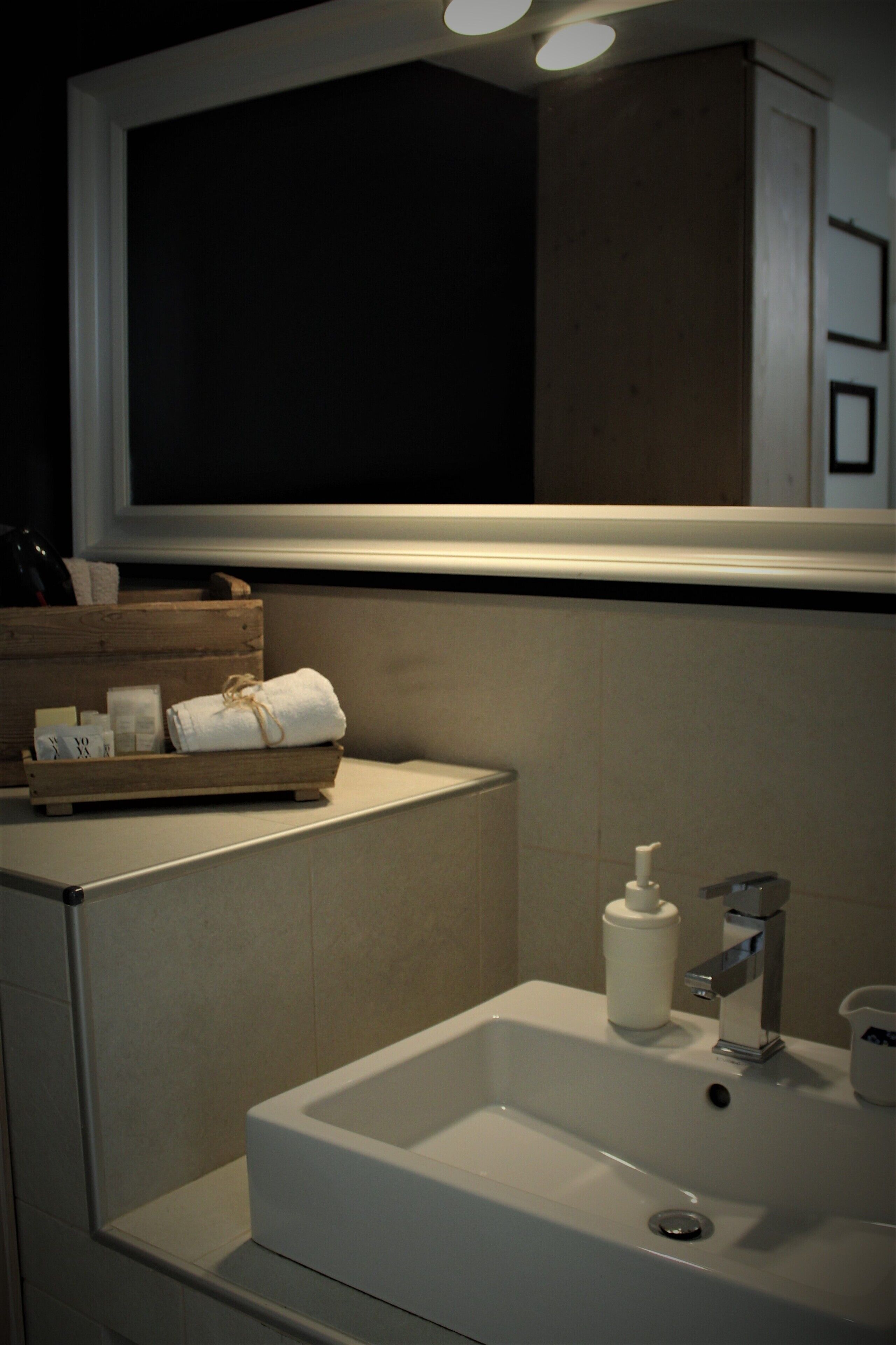 A bathroom with a white sink, a bottle of hand soap, and a wooden tray with towels.