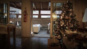 A cozy room with a wooden ceiling, a Christmas tree, a dining area with a table and chairs, and a view through a glass door to an outdoor seating area. - B&B Ca' Virò (Albosaggia)