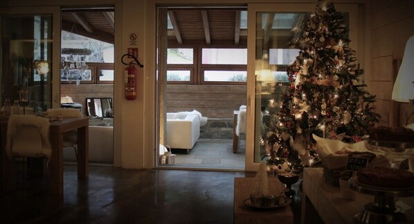 Una habitación acogedora con techo de madera, un árbol de Navidad, un comedor con mesa y sillas, y vistas a una zona de estar exterior a través de un ventanal.