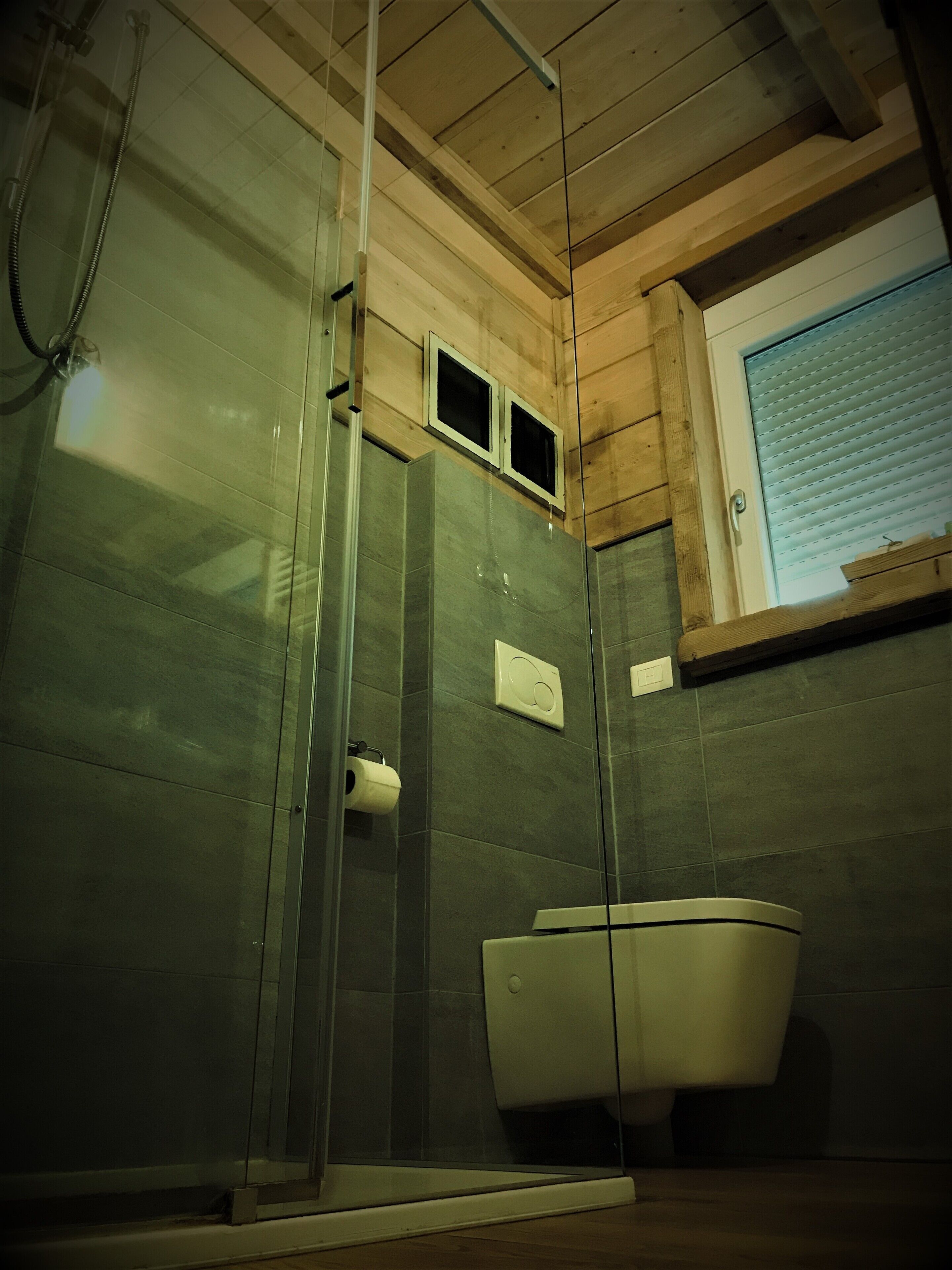 Un baño con cabina de ducha de vidrio, inodoro y ventana con persianas.