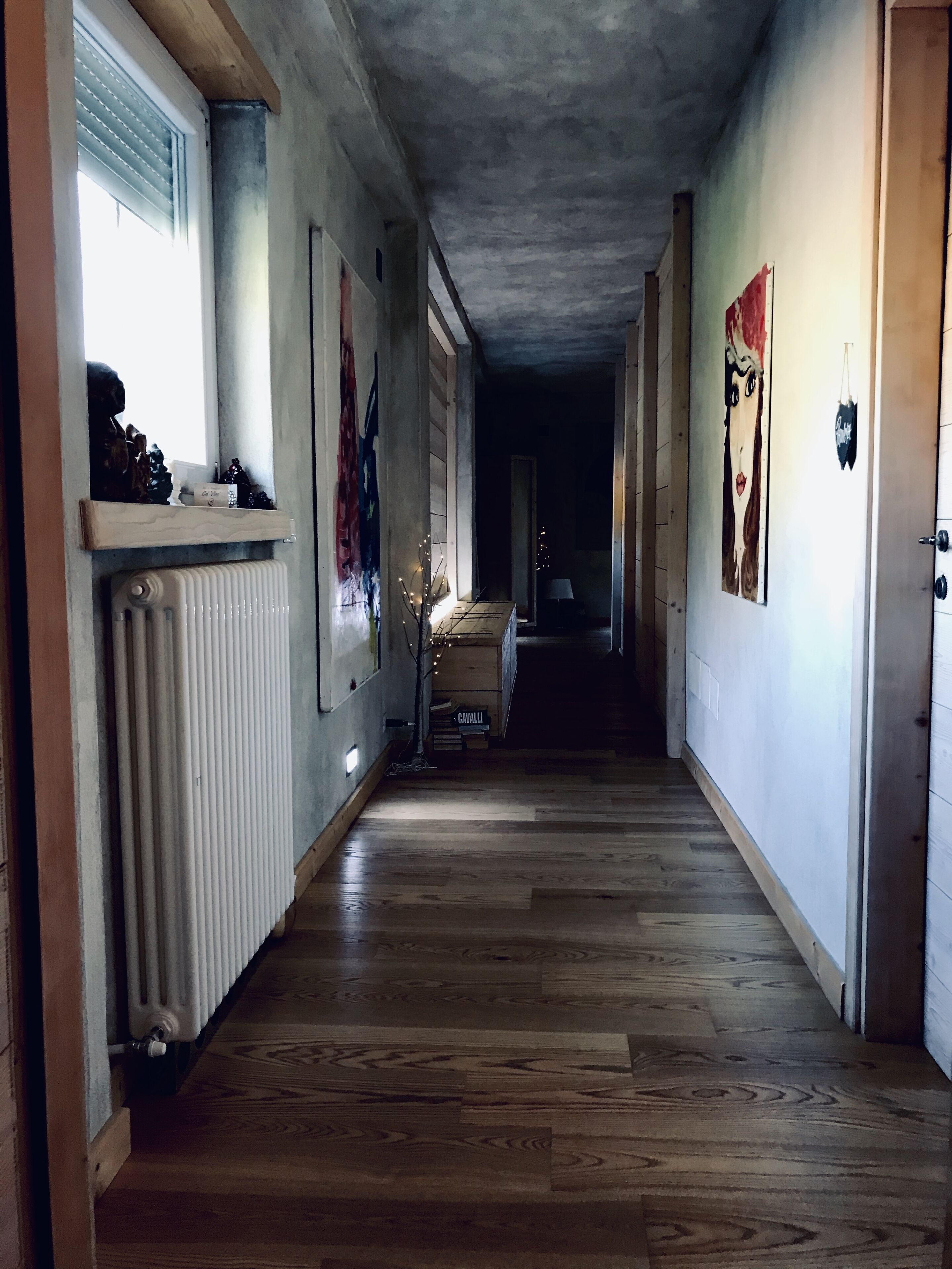 Un pasillo con suelo de madera, un radiador y una estantería con adornos.