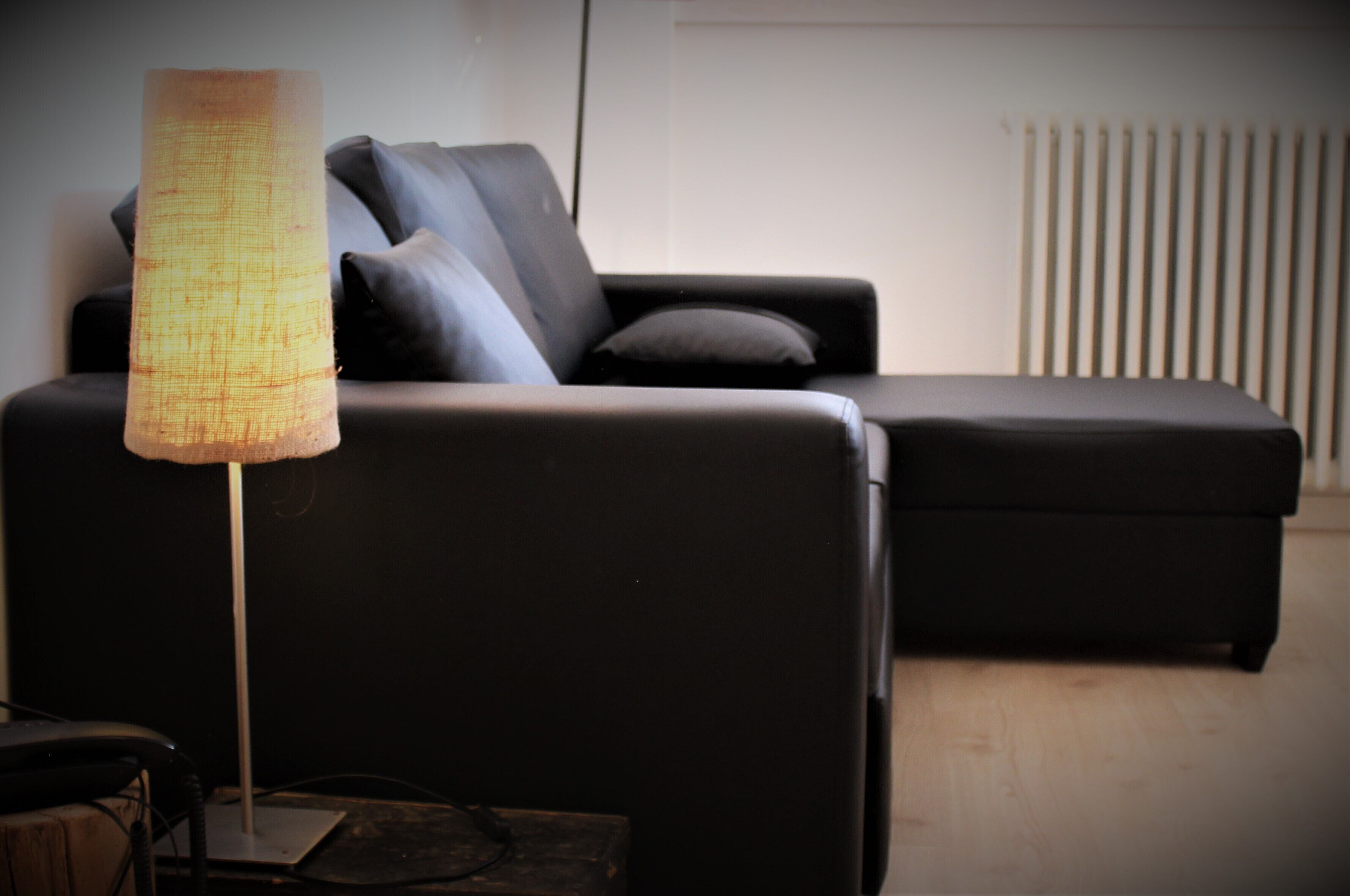 Una sala moderna con un sofá negro, una lámpara de pie y un radiador.