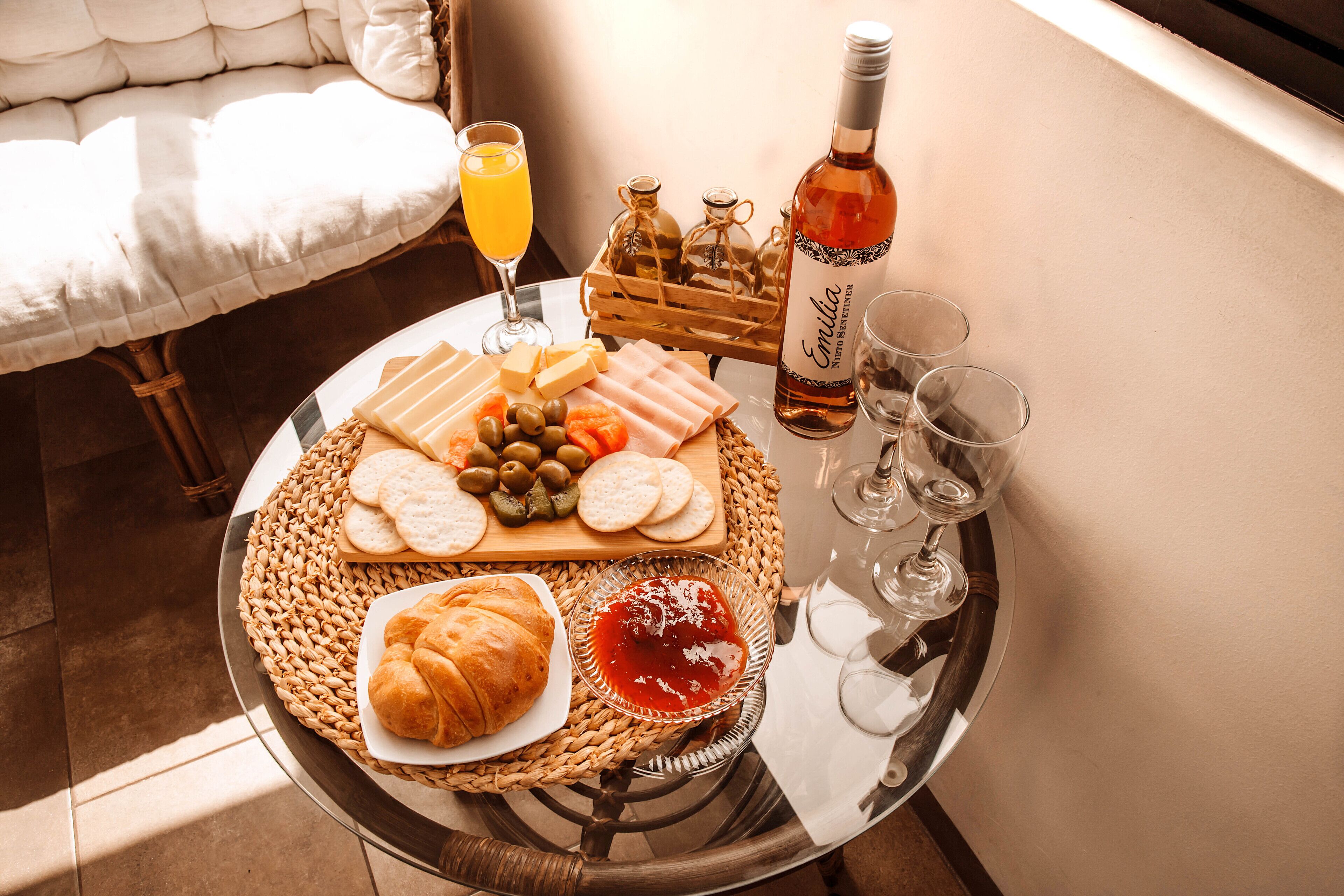 A breakfast table with croissants, cheese, olives, bread, and jam. There are also wine glasses, a bottle of wine, and a glass of orange juice.