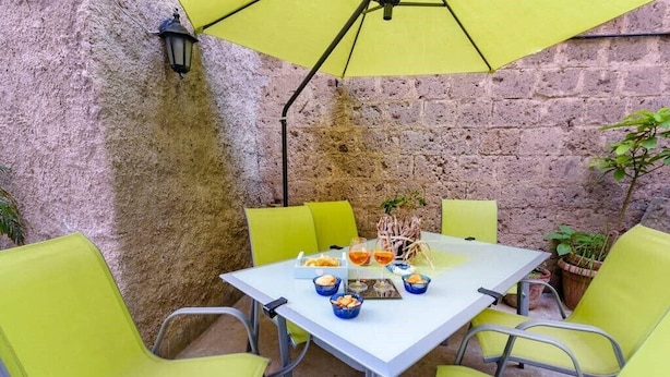 An outdoor patio with a white table, yellow chairs, and a yellow umbrella.
