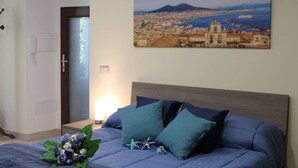 A bedroom with a bed, a wall-mounted painting of a coastal cityscape, and a bouquet of flowers on the bed.