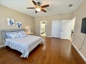 Une chambre à coucher comprenant un lit, un ventilateur de plafond, une table de chevet et une porte donnant sur une autre pièce.