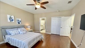A bedroom with a bed, a ceiling fan, a nightstand, and a door leading to another room.