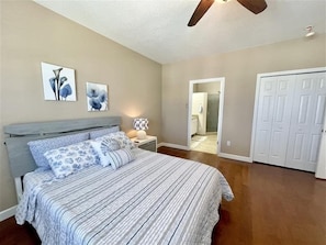 A bedroom with a bed, nightstands, a ceiling fan, and a door leading to a bathroom.