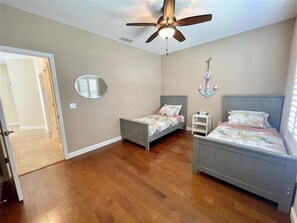 A bedroom with two beds, a ceiling fan, a mirror, and a small table. - Beach Bird House- Walk to the Beach! 4224 Oriole (Wilbur by the Sea)