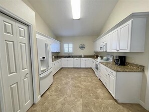 A compact kitchen with white cabinetry, a refrigerator, a stove, and a coffee maker. - Beach Bird House- Walk to the Beach! 4224 Oriole (Wilbur by the Sea)