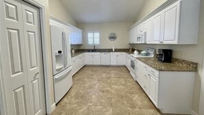 A compact kitchen with white cabinetry, a refrigerator, a stove, and a coffee maker.