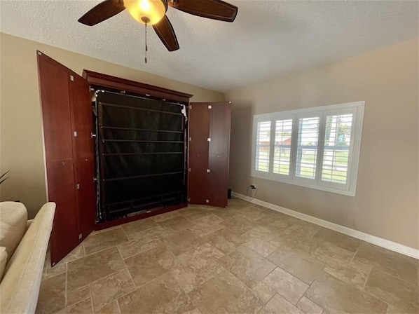 A room with a large sliding door, a ceiling fan, and a window with blinds.