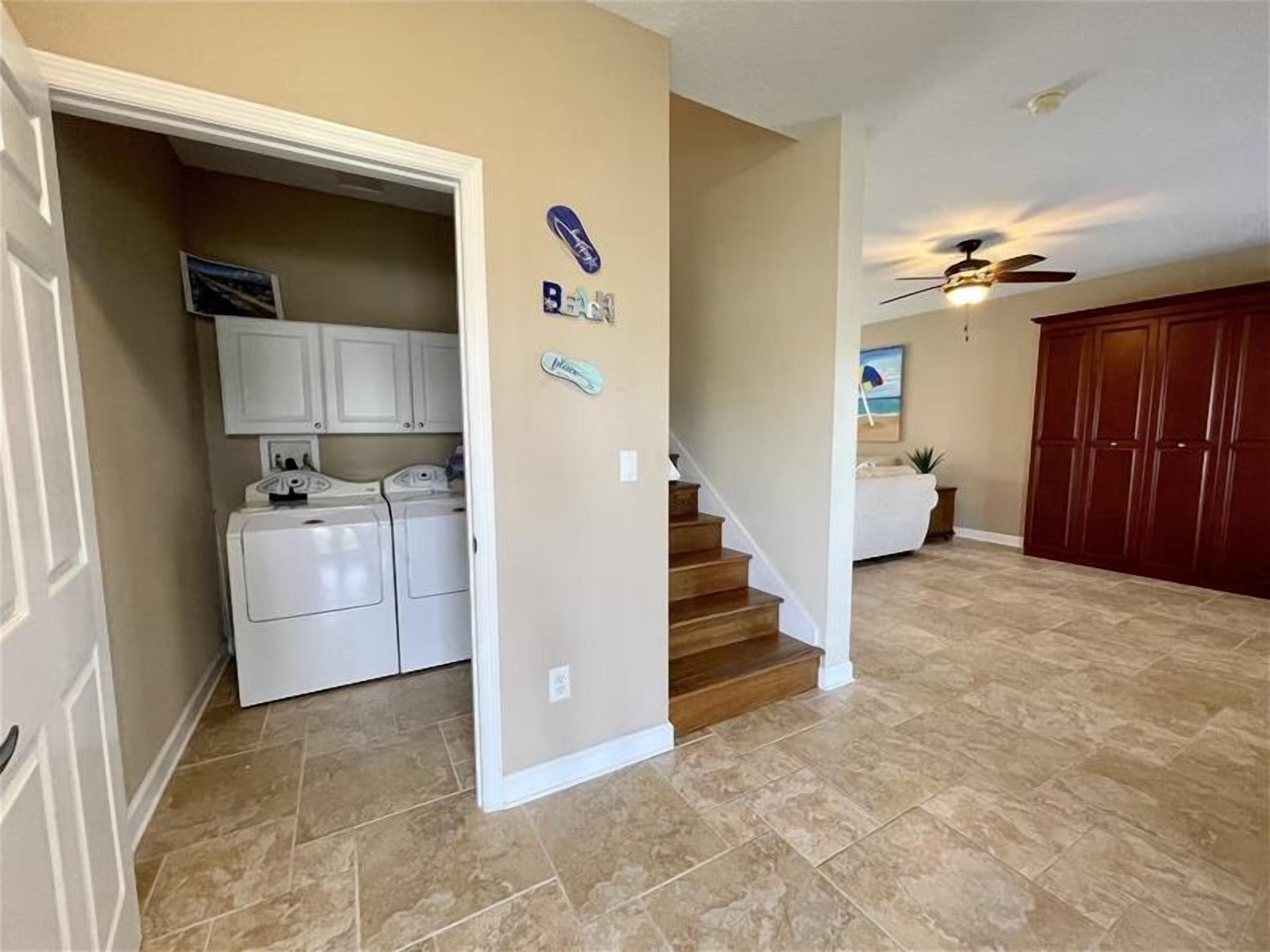 A laundry area with a washing machine and dryer, a staircase leading to a bedroom, and a ceiling fan.