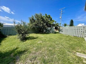 A backyard with a wooden fence, a small tree, and a grassy lawn. - Beach Bird House- Walk to the Beach! 4224 Oriole (Wilbur by the Sea)