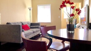 A living room with a grey sofa, red pillow, and a dining table with chairs. - Modern and Perfect Self Contained 4B/2BA Home +  Parking + BART (El Cerrito)