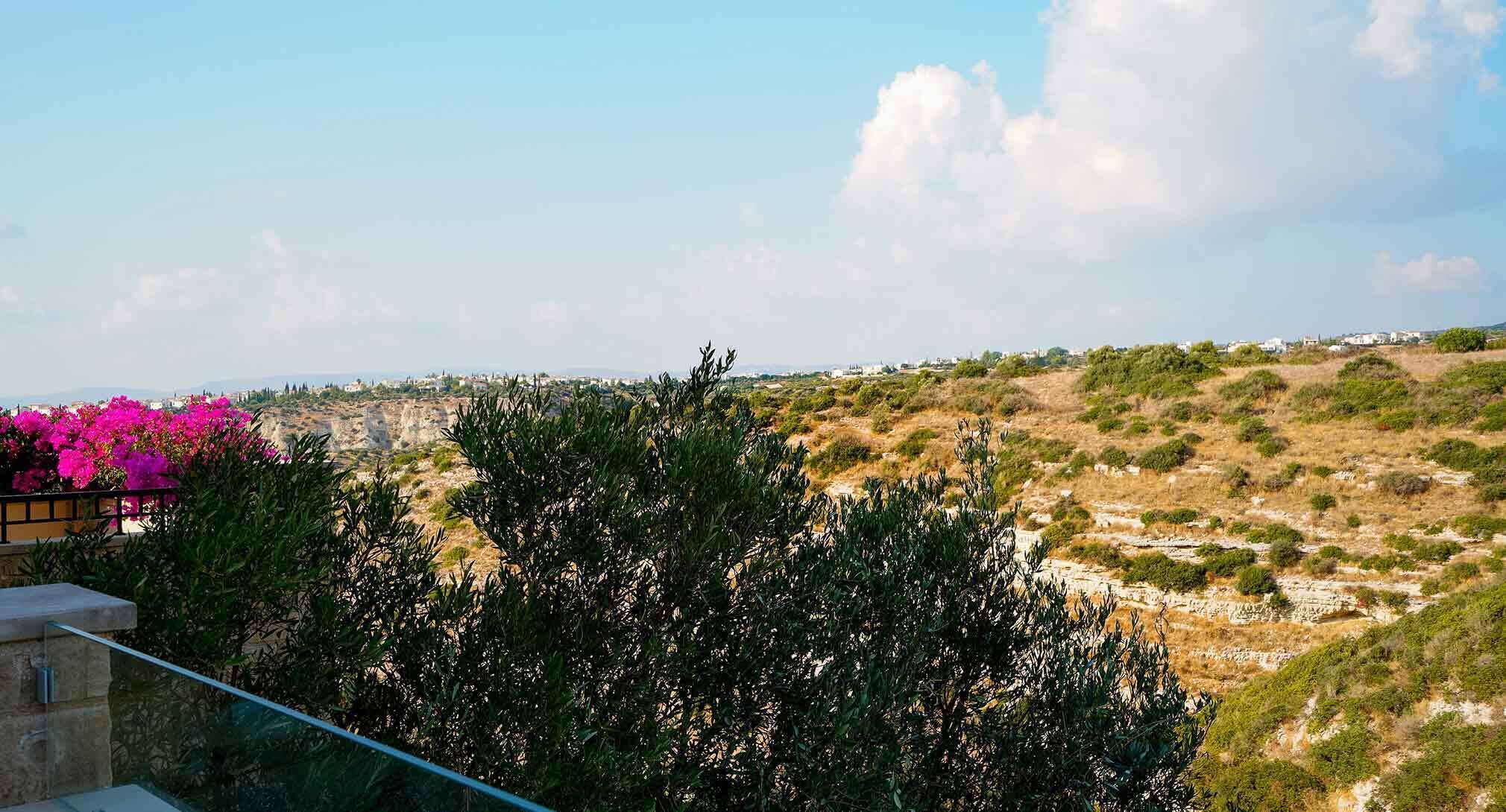 A view of a coastal landscape with a balcony overlooking a rocky terrain and a distant town.