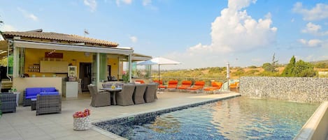 A poolside area with a tiled deck, outdoor seating, and a view of the landscape.