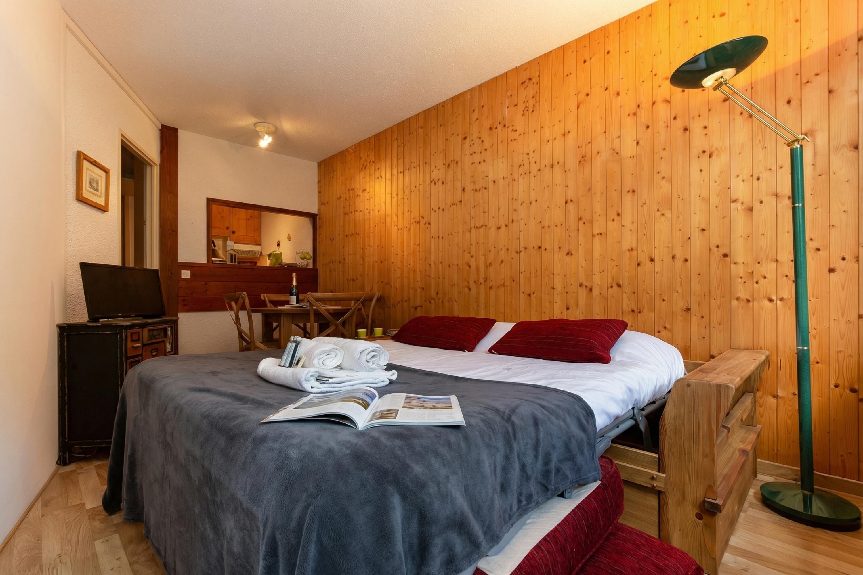 Um quarto aconchegante com uma cama, uma escrivaninha com computador, uma parede de madeira e um abajur.