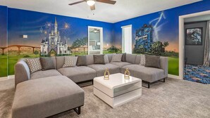Ein Wohnzimmer mit einer Eckcouch, einem Couchtisch und einem Wandbild mit Schloss und Feuerwerk.