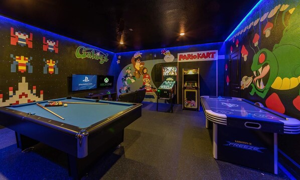 A pool table, a Nintendo 64 arcade, and a Mario Kart arcade in a room with colorful murals and neon lighting. - 8BR ChampionsGate | Theater, Arcade & Pool (Davenport)