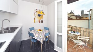 A compact kitchen with a sink and a dining area with a table and chairs. There's a balcony with a table and chairs, and a cityscape view.