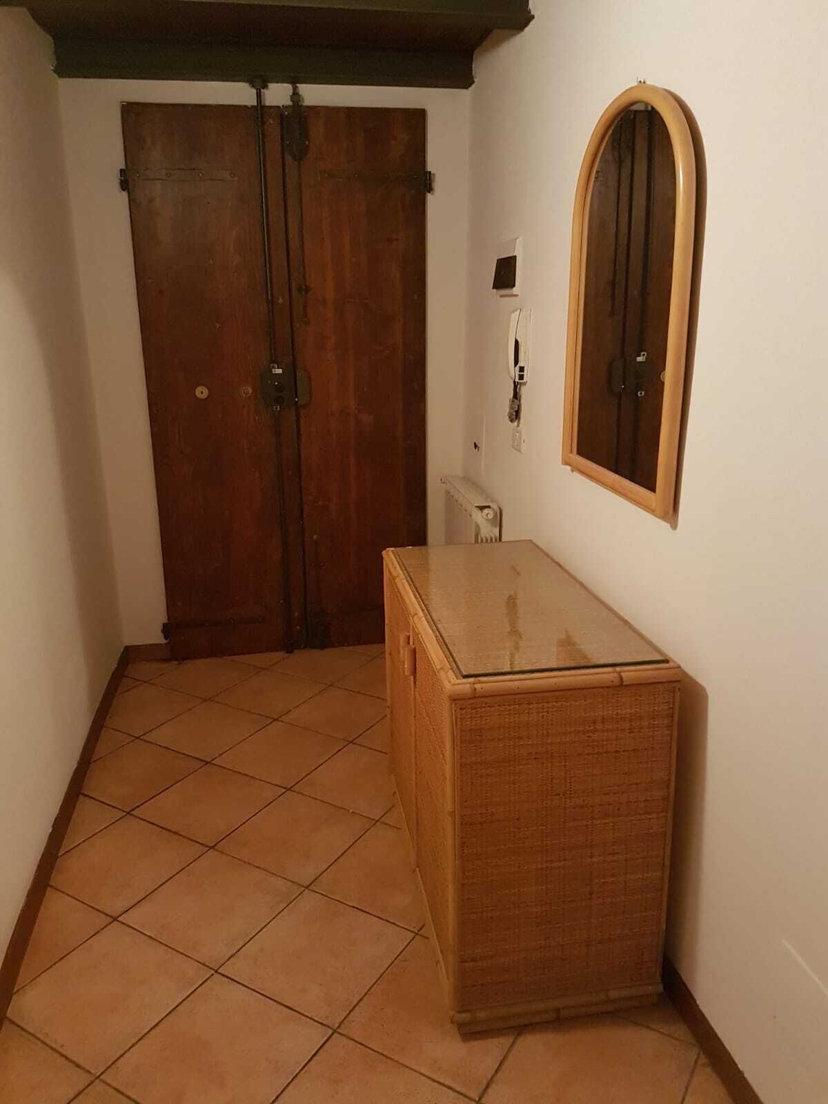 A room with a wooden wardrobe, a small cabinet, and a mirror on the wall.