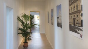 A hallway with a potted plant, framed pictures on the walls, and a door at the end leading to another room.