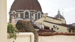 A balcony with a table, chairs, and a bottle of wine. In the background, there is a building with a dome and another building with a smaller dome.