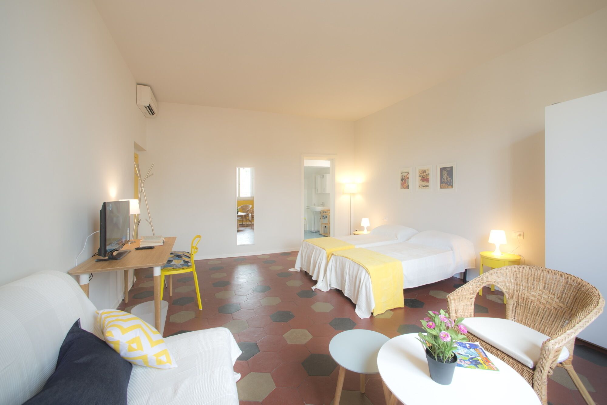 A hotel room with a bed, a desk with a computer, a chair, a sofa, and a small table with a plant.