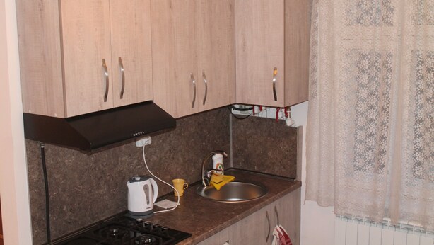 A kitchen with wooden cabinets, a black range hood, a stainless steel sink, and a patterned window curtain.