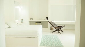 Een minimalistische slaapkamer met een bed, een stoel, een klein tafeltje en een raam.