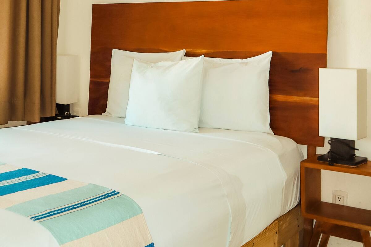 Een net opgemaakt bed met witte lakens en een blauw-witte strepen deken.