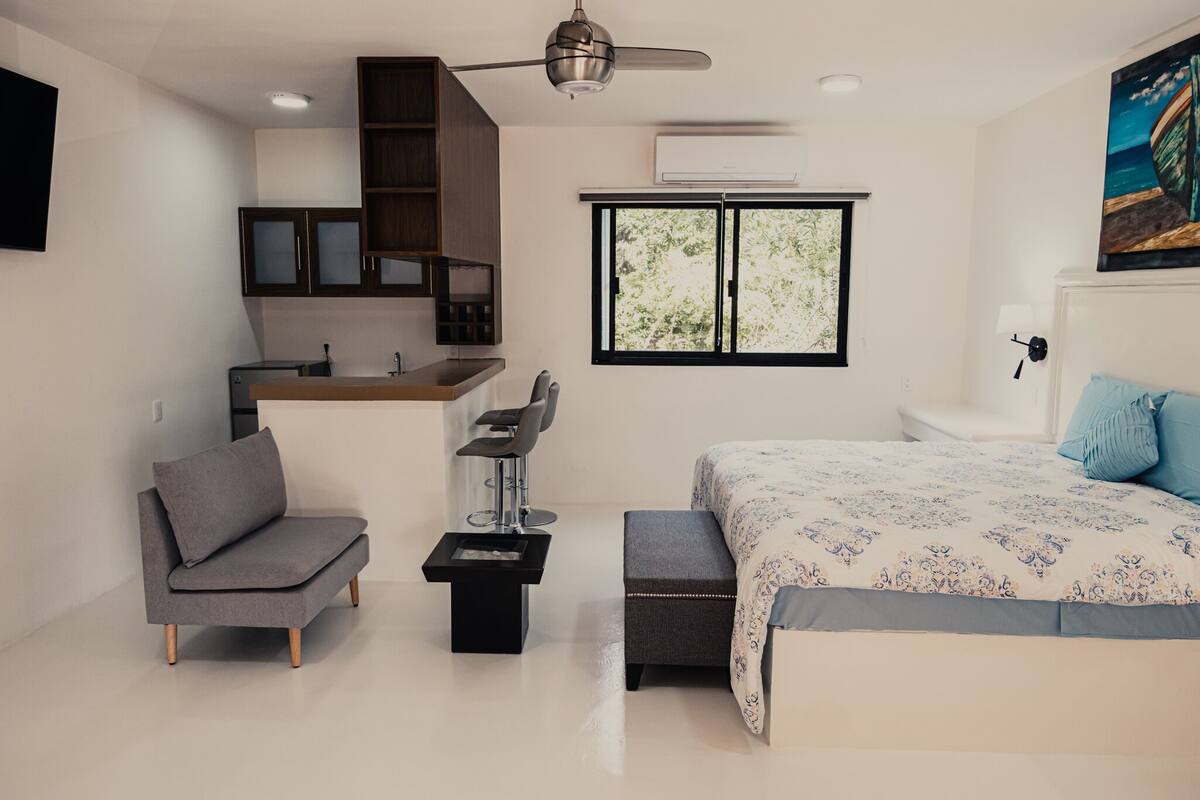 Een moderne slaapkamer met een bed, een bureau, een stoel en een kitchenette.