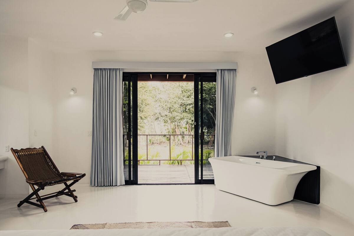 Een moderne badkamer met een vrijstaand bad, een stoel en een groot raam met gordijnen.