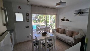 A room with a white sofa, a dining table with chairs, a small pool visible through the glass door, and a ceiling light fixture.
