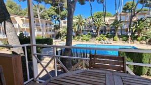 A pool area with a wooden deck, surrounded by palm trees and a clear blue sky.